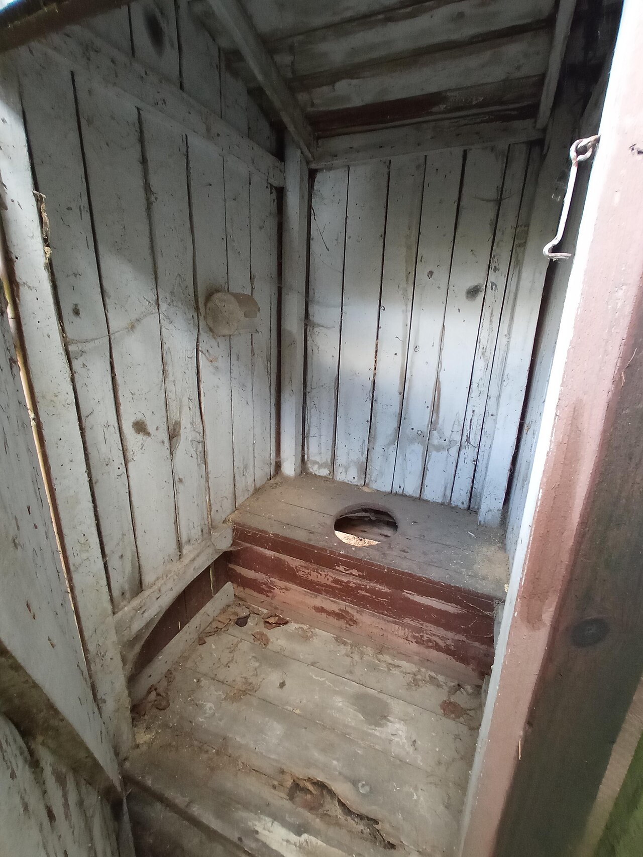 Interior of a simple outdoor composting toilet with wooden box seat and hole
