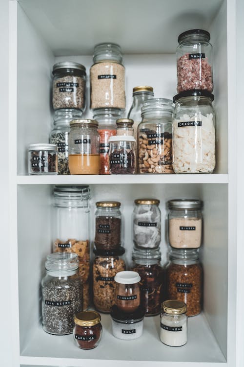 Glass jars filled with dried foods on a white wooden pantry shelf