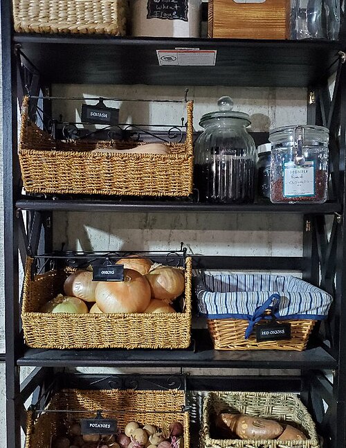 Homestead pantry shelves with labeled baskets of onions, potatoes, and glass jars of dry goods