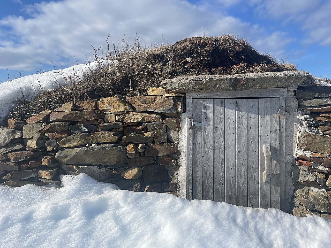 Stone-lined hillside root cellar with timber door, snow on the ground